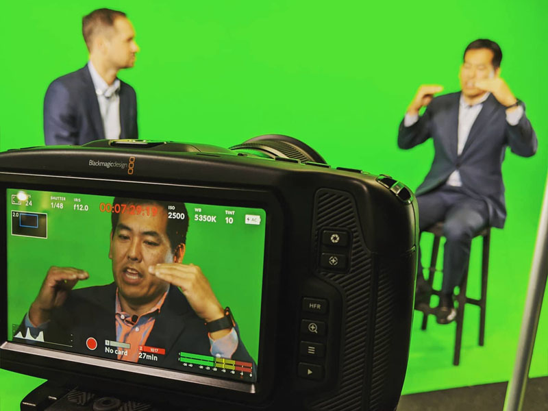 a picture if businessmen shooting in front of green screen interviewing with camera