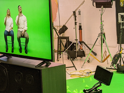 a picture of actor and actress shooting in front of green screen with chairs kino flo lights tv monitor sound speaker camera recording