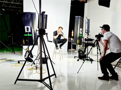 a picture of actor posing on stool shooting in stuido white seamless with cameraman kino flo lights camera extension cords